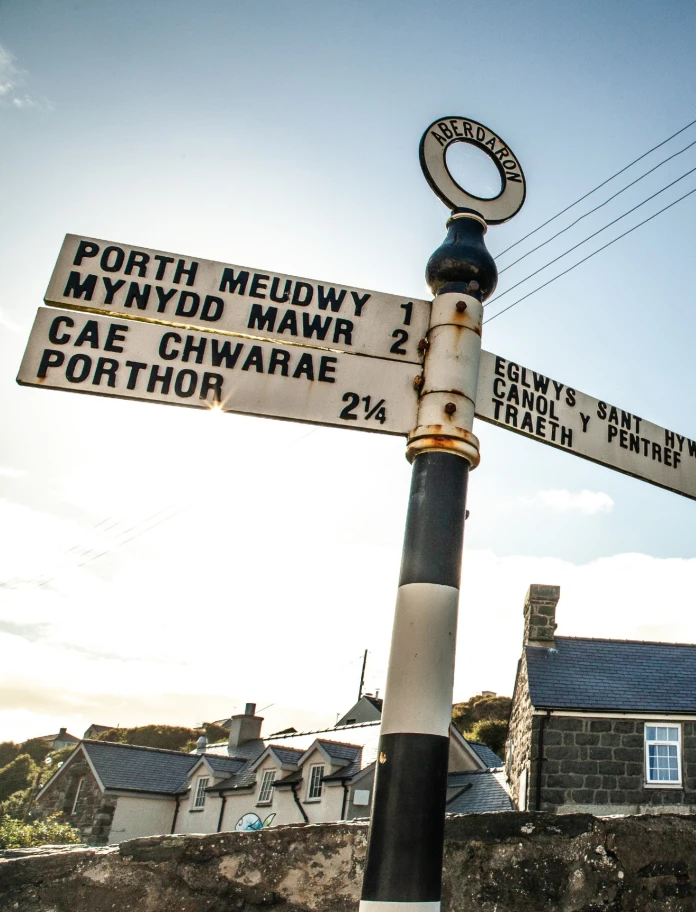 Welsh language road sign in foreground with cottages behind.