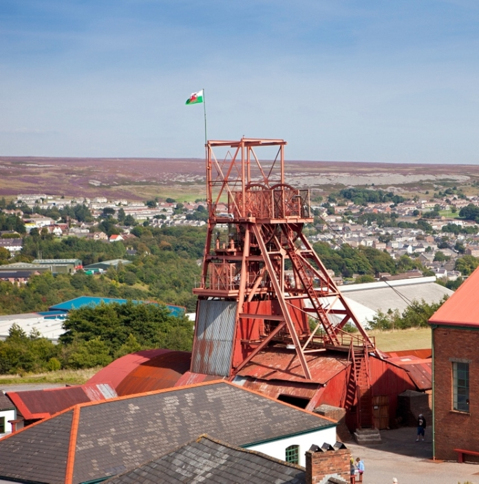 A view of a forecourt with a red pit wheel and a red building in Blaenavon.