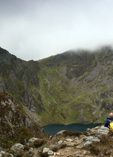 A group of people sat looking at Llyn Cau from the Minffordd Path, Cader Idris, Snowdonia with Craig Cau (left) and Penygadair (right).