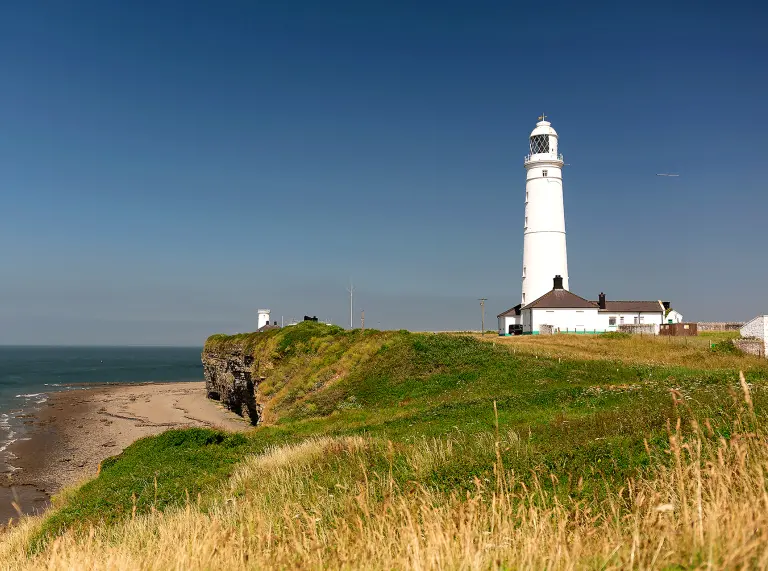 A white lighthouse on a cliff edged coastline.