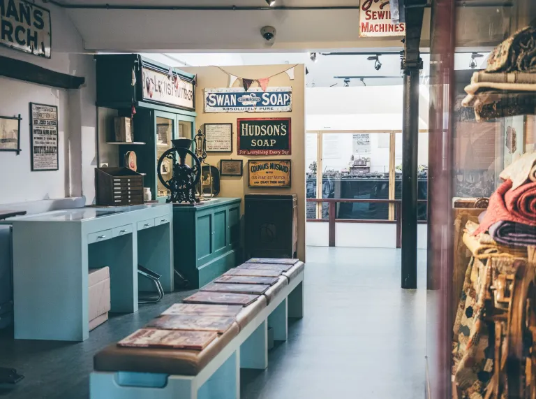 Vintage interior in museum with retro signs, old soap ads, and sewing machines. Displayed benches and various textiles.