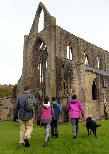 A group people and a dog by a ruined abbey.