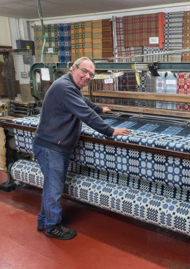 A weaver working on a weaving loom making traditional Welsh geometric colourful fabrics
