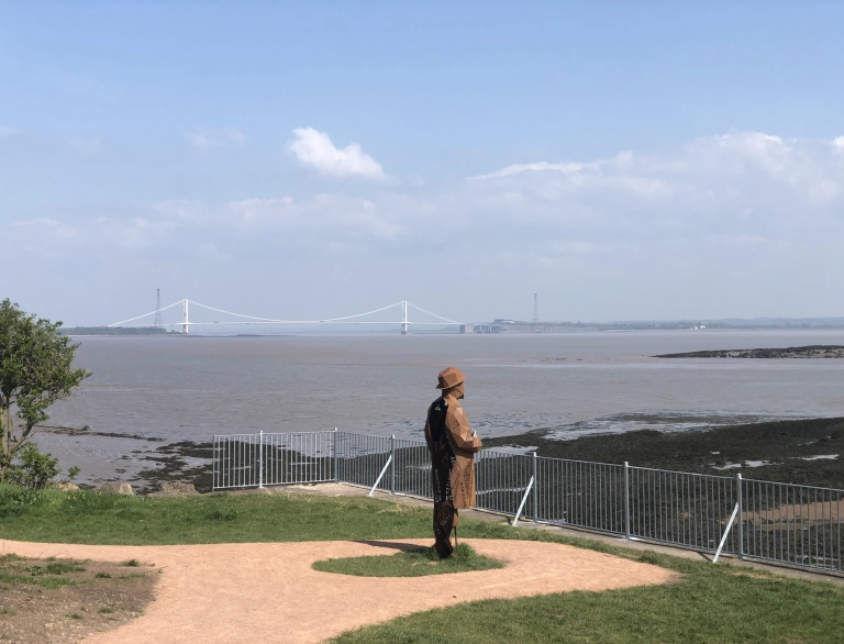 A tall metal sculpture of a man looking out over an estuary.