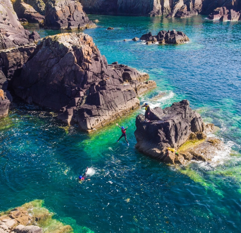 People jumping off rocks in the sea wearing full safety gear.