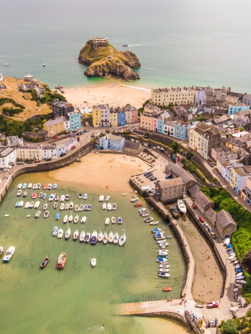 Aerial view of a harbour, two beaches and pastel coloured houses.