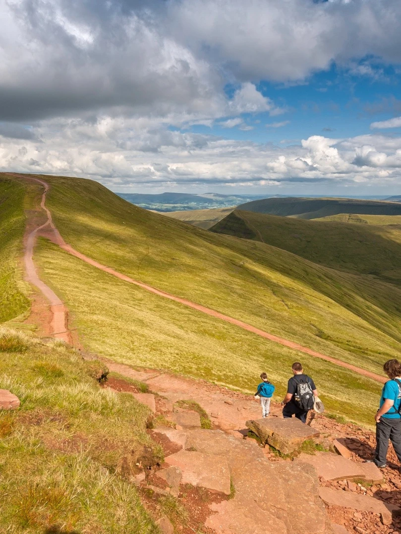child and two adult walkers approaching summit of mountain.