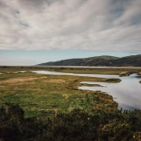 Dyfi estuary with grass on each side and hills in the background under moody skies