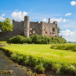 Ruined castle on a sunny summer day with stream and grassy bank in the foreground