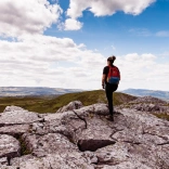 Woman hiker standing on hill, against a blue sky, looking out across the green, mountainous landscape of the Brecon Beacons, Mid Wales.