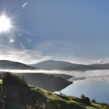Person looking out over the mountains and a lake in the early morning.