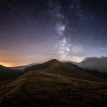 Dark sky full of stars above the mountain landscape of the Bannau Brycheiniog (Brecon Beacons) with the orange glow of the setting sun on the horizon.