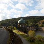 An ornate stone dam next to a footpath and narrow road.