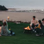 family sat on cliff over looking the sea with camp fire.
