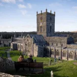 exterior of cathedral and two people sat on bench.
