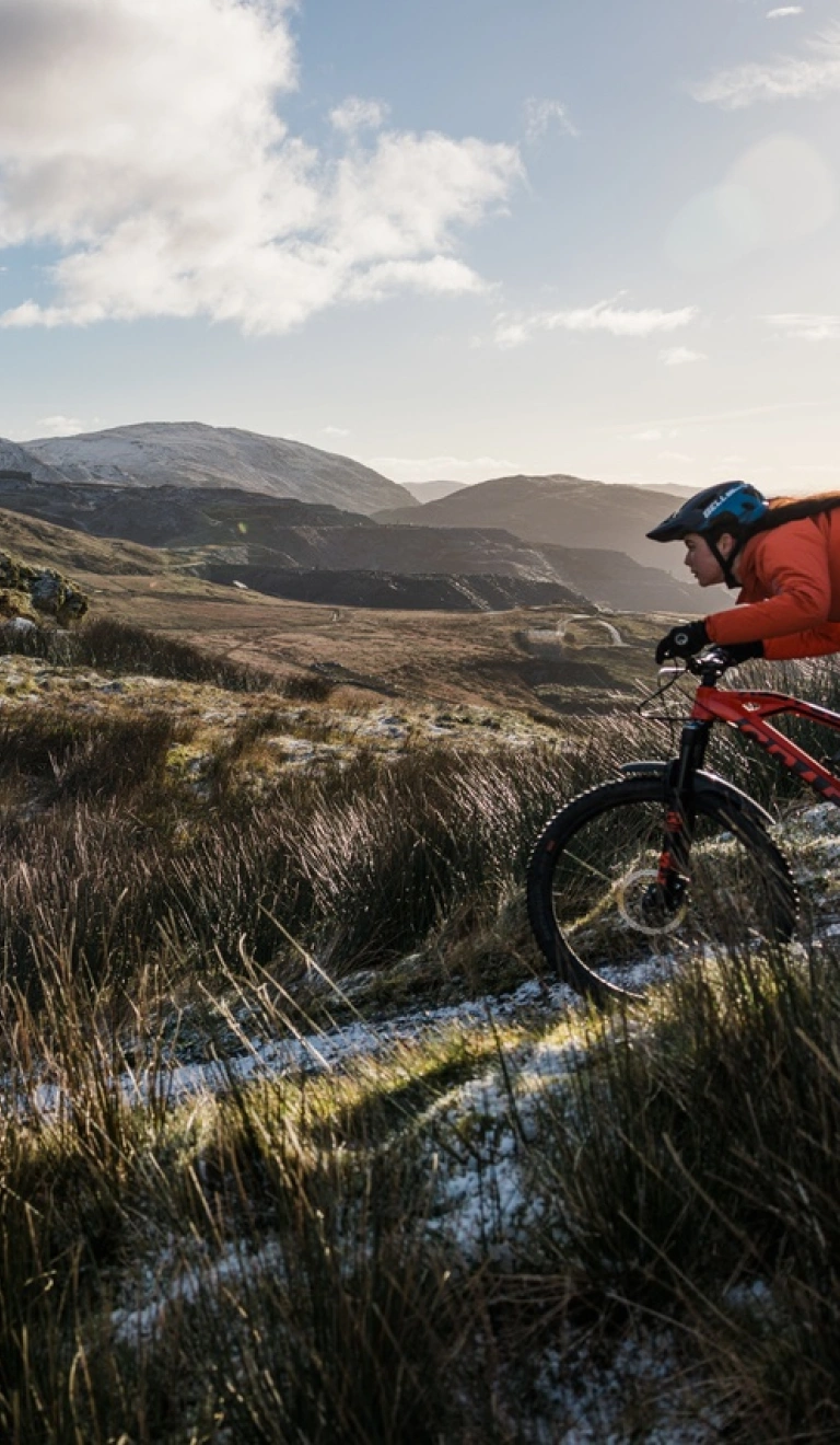 Three riders on mountain bikes riding a mountain trail with a view of mountain peaks in the background