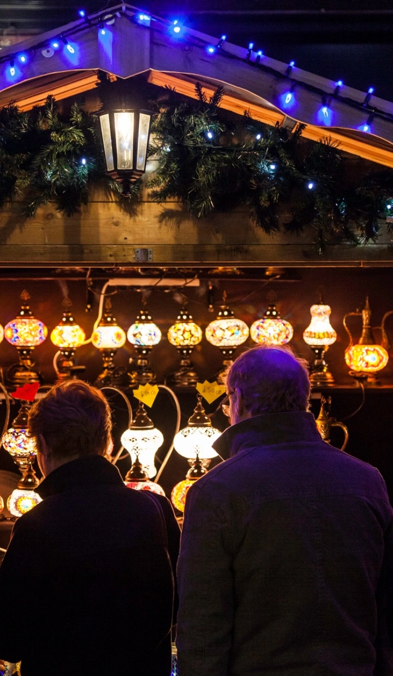 nighttime shot of Christmas market stall selling lamps with people in the foreground.